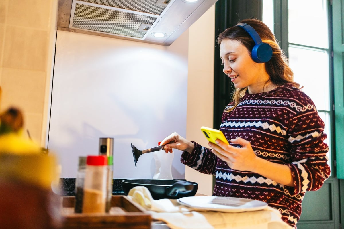A young woman cooking breakfast in a modern kitchen while listening to music