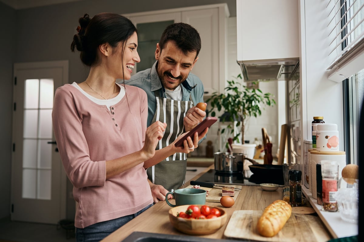 A couple reading a recipe on a phone while cooking together in the kitchen