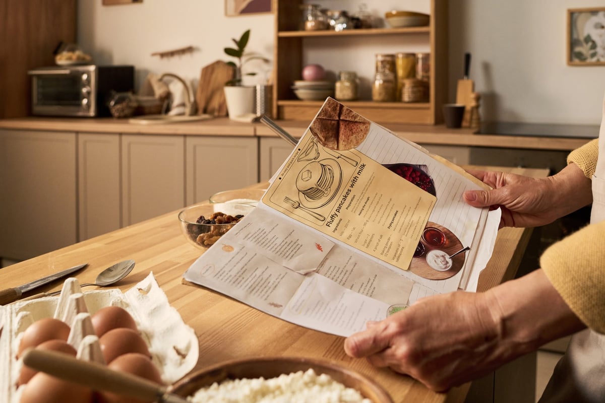 A woman arranging ingredients on a kitchen counter while following a recipe booklet